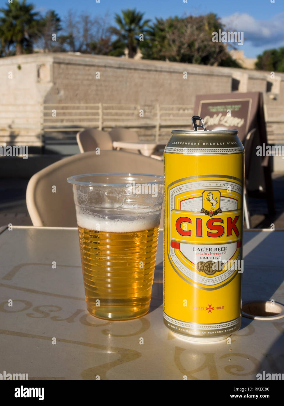 A can of the local lager beer brand Cisk and a plastic glass in an ope air bar in Malta with the city fortifications of Mdina in the background Stock Photo