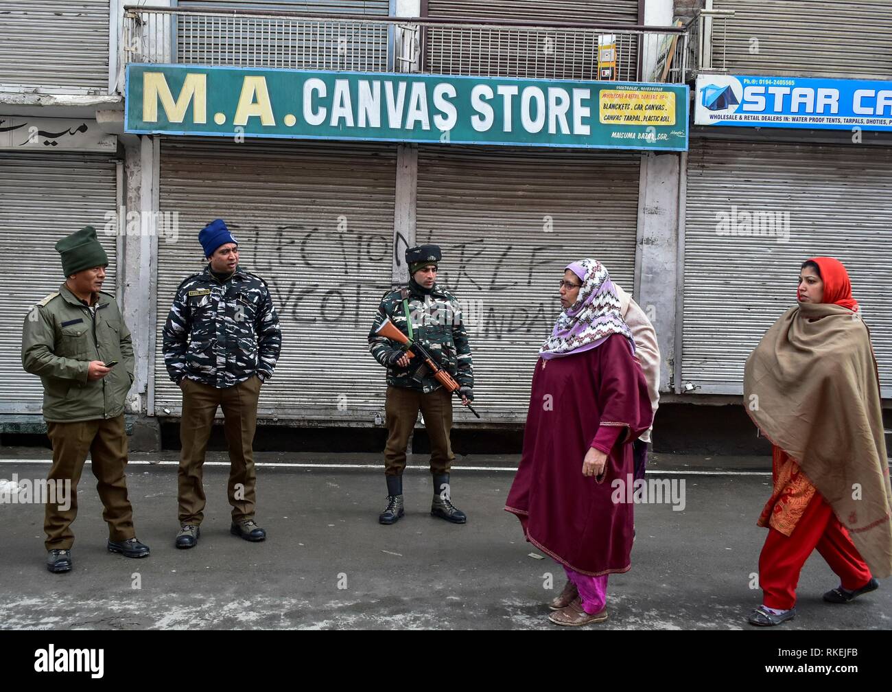 February 11, 2019 - Srinagar, J&K, India - Kashmiri women walk past paramilitary troopers standing alert during restrictions in Srinagar, Indian administered Kashmir. Curfew-like restrictions have been imposed in parts of Srinagar city in the wake of a call for strike by separatist groups to commemorate the death anniversary of Maqbool Bhat, the Jammu and Kashmir Liberation Front (JKLF) founder who was hanged on Feb 11, 1984 in Delhi's Tihar Jail. The separatist leaders and activists staged a protest demanding back the mortal remains of slain Maqbool Bhat. (Credit Image: © Saqib Majeed/SOPA I Stock Photo