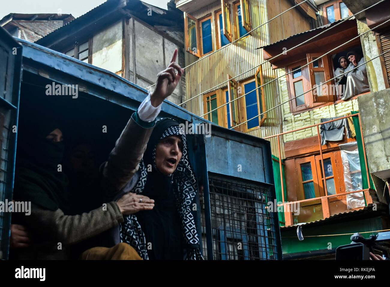 February 11, 2019 - Srinagar, J&K, India - Kashmiri women watch from the window as a member of the Muslim Khawateen Markaz shouts pro-freedom slogans from a police vehicle after being detained during a protest in Srinagar, Indian administered Kashmir. Curfew-like restrictions have been imposed in parts of Srinagar city in the wake of a call for strike by separatist groups to commemorate the death anniversary of Maqbool Bhat, the Jammu and Kashmir Liberation Front (JKLF) founder who was hanged on Feb 11, 1984 in Delhi's Tihar Jail. The separatist leaders and activists staged a protest demandi Stock Photo