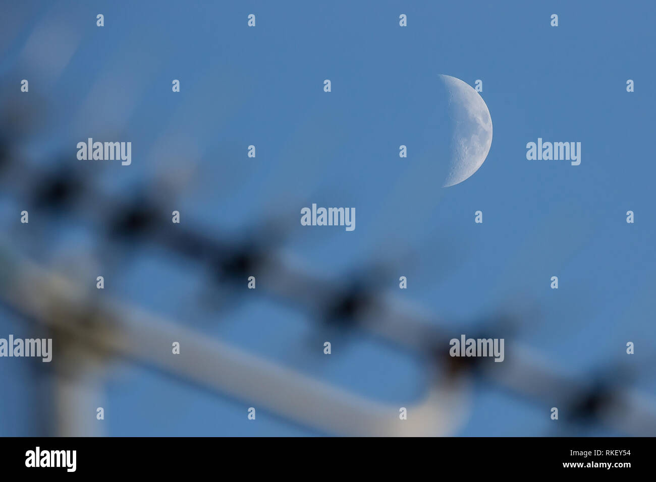Kidderminster, UK, 11th February, 2019. UK weather: almost clear blue skies reveal a waxing crescent moon as the day draws to an end. It will be a chilly night with temperatures not rising above 2 degrees celsius. The moon can be seen rising above the television aerial on a UK house roof. Credit: Lee Hudson/Alamy Live News Stock Photo