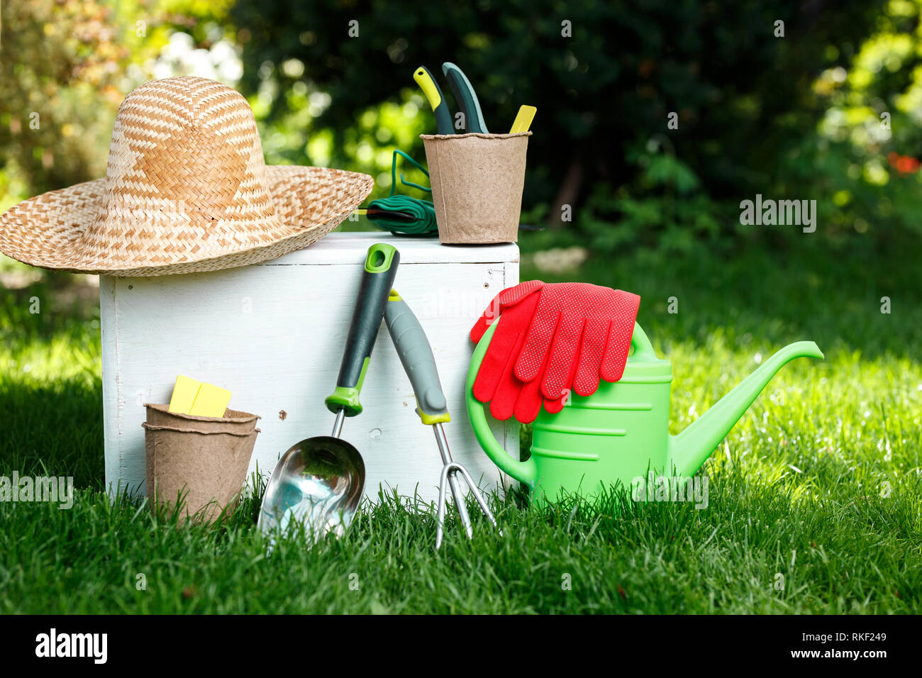 Gardening tools, gloves, straw hat and white wooden box on green grass, garden maintenance and hobby concept Stock Photo