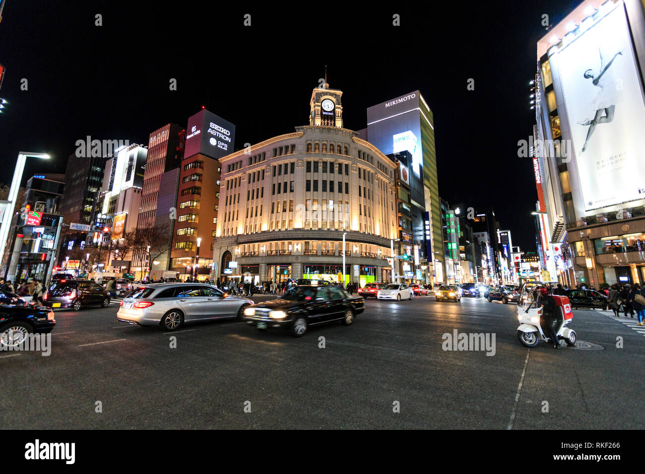 Tokyo, Ginza, night. 4-chome intersection with traffic and taxis passing by, motion blur, and in background the Wako Department store and others. Stock Photo