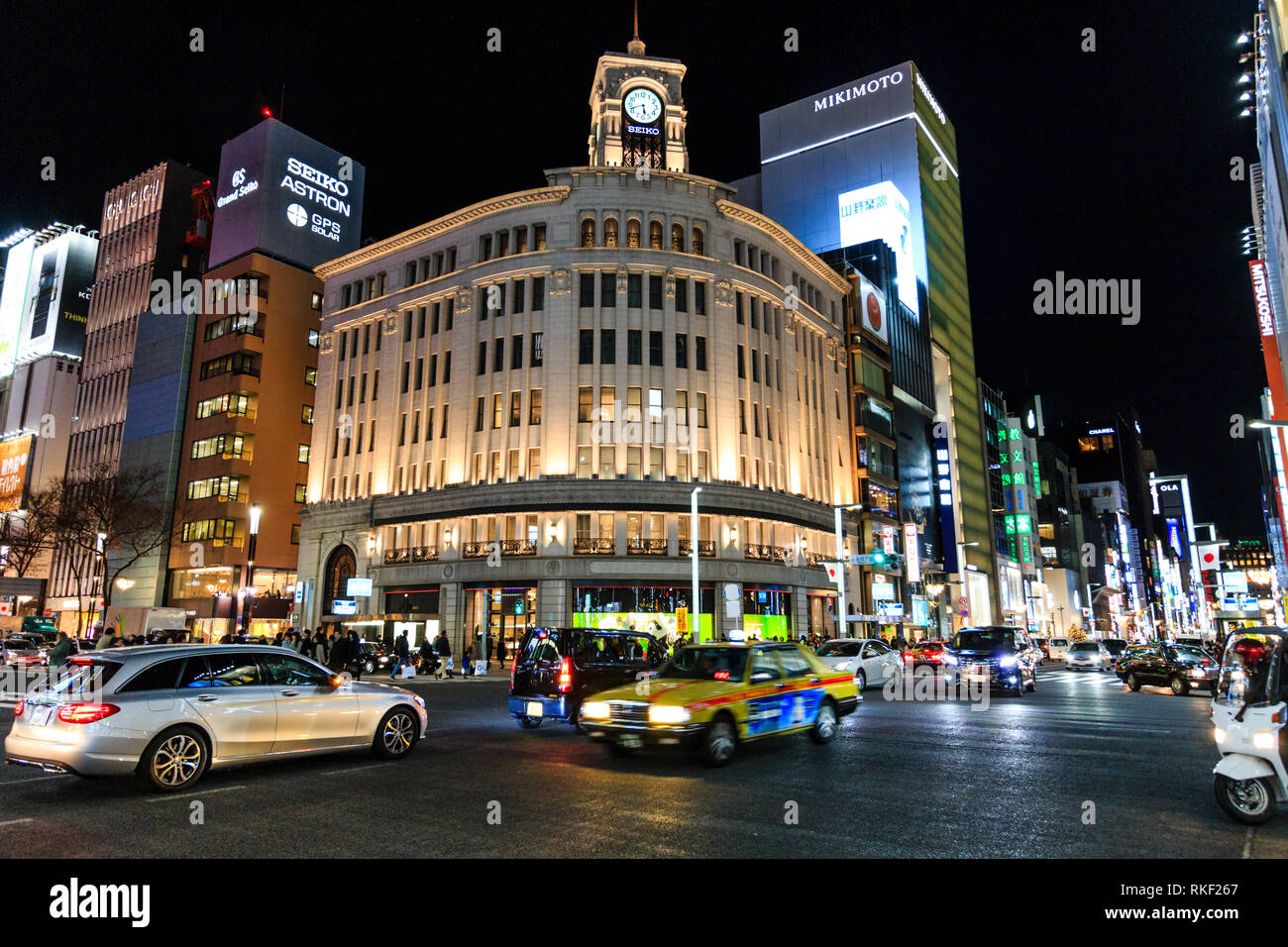 Tokyo, Ginza, night. 4-chome intersection with traffic and taxis passing by, motion blur, and in background the Wako Department store and others. Stock Photo