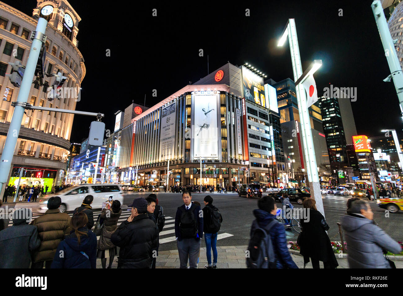 Tokyo, Ginza, night. Wide angle view of people waiting at pedestrian crossing, Wako and Mitsukoshi department stores opposite. Traffic, motion blur. Stock Photo