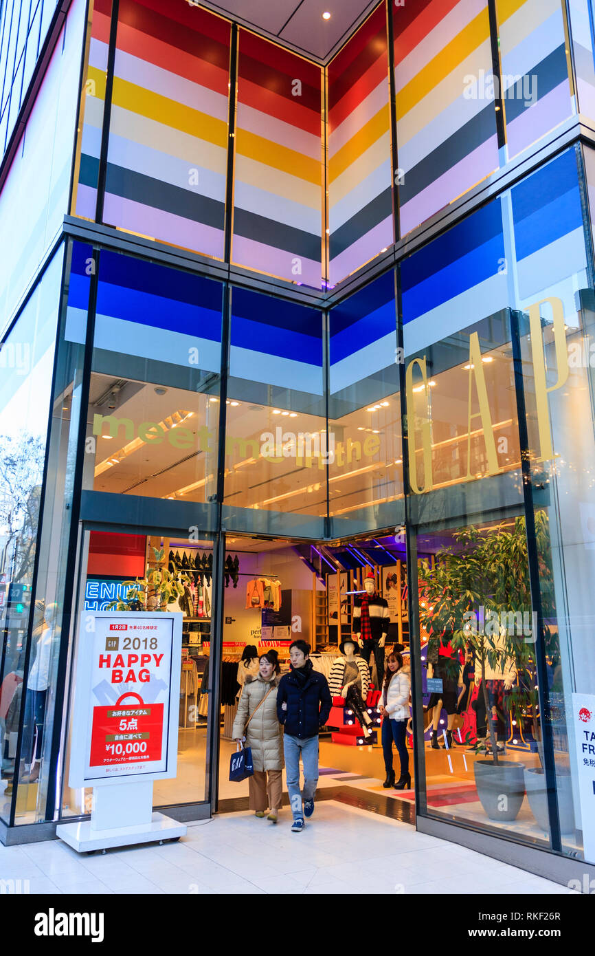 Tokyo, Ginza, daytime. Entrance to the flagship Gap superstore at Chome 4. Young Japanese smiling couple leaving store, passing a Happy Bag sign. Stock Photo
