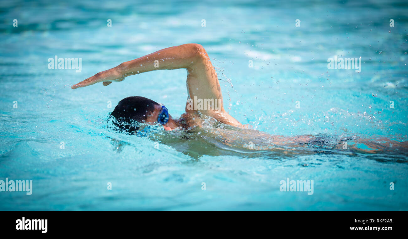 Man swimmer swimming crawl in a blue water  pool. Portrait of an athletic young male triathlete swimming crawl wearing swimming goggles. Triathlete tr Stock Photo
