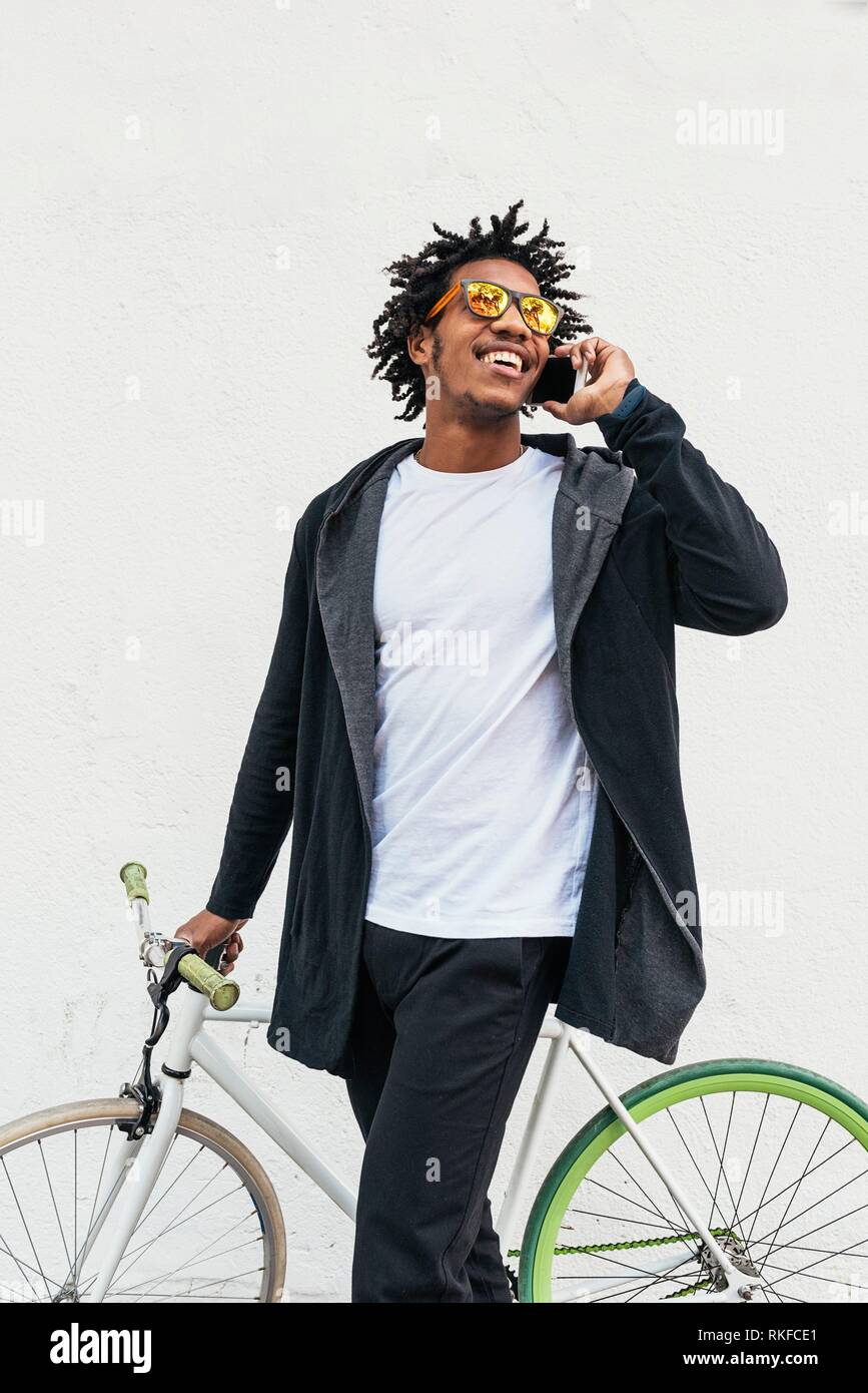 Afro young man using mobile phone and fixed gear bicycle in the street. Stock Photo