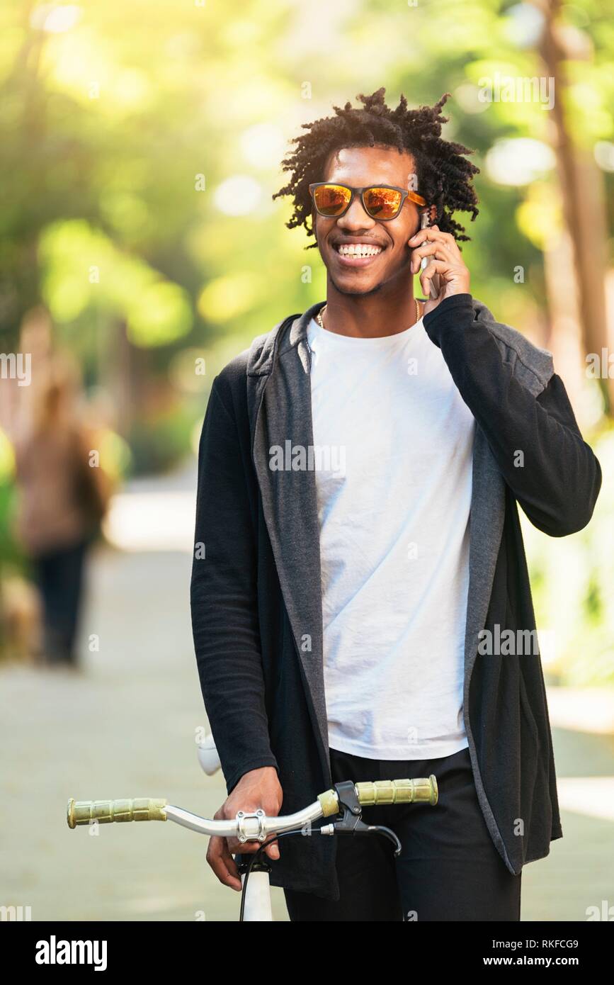 Afro young man using mobile phone and fixed gear bicycle in the street. Stock Photo