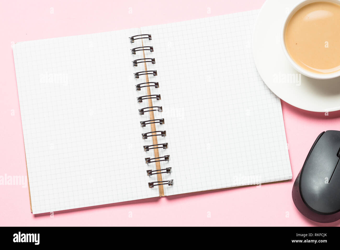 Office workplace with notepad, coffee cup and mouse on pink desk. Stock Photo
