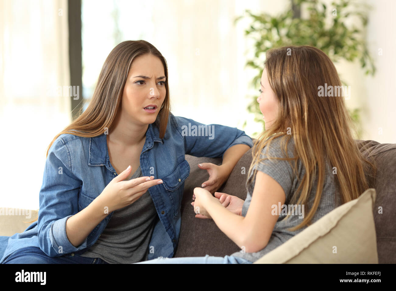 Serious women talking sitting on a couch in the living room at home Stock Photo