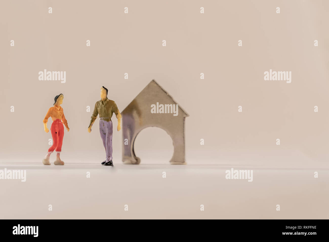 Miniature woman and man figure standing next to house made of coin holder with no coins. Shallow depth of field background. Family budget, mortgage an Stock Photo