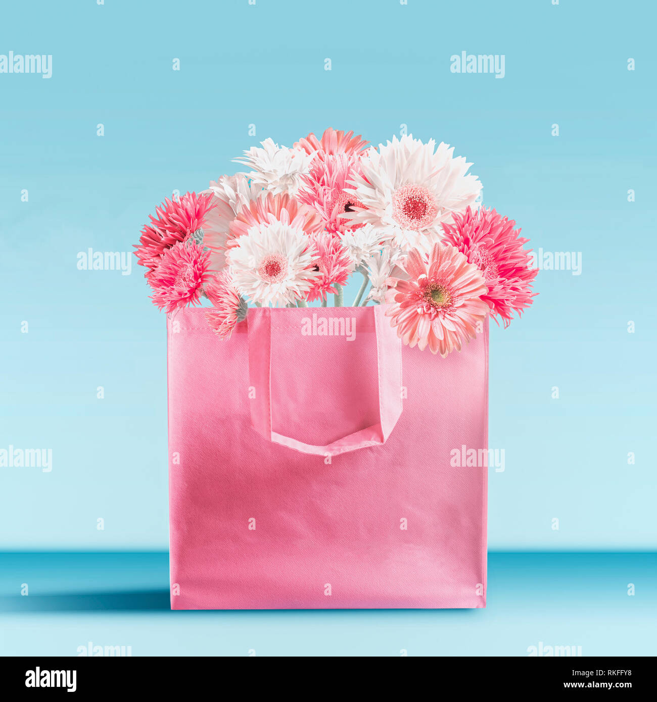 Pastel pink shopping bag with gerbera daisies flowers bunch standing on table at turquoise blue wall background. Branding mock up. Copy space. Summer  Stock Photo