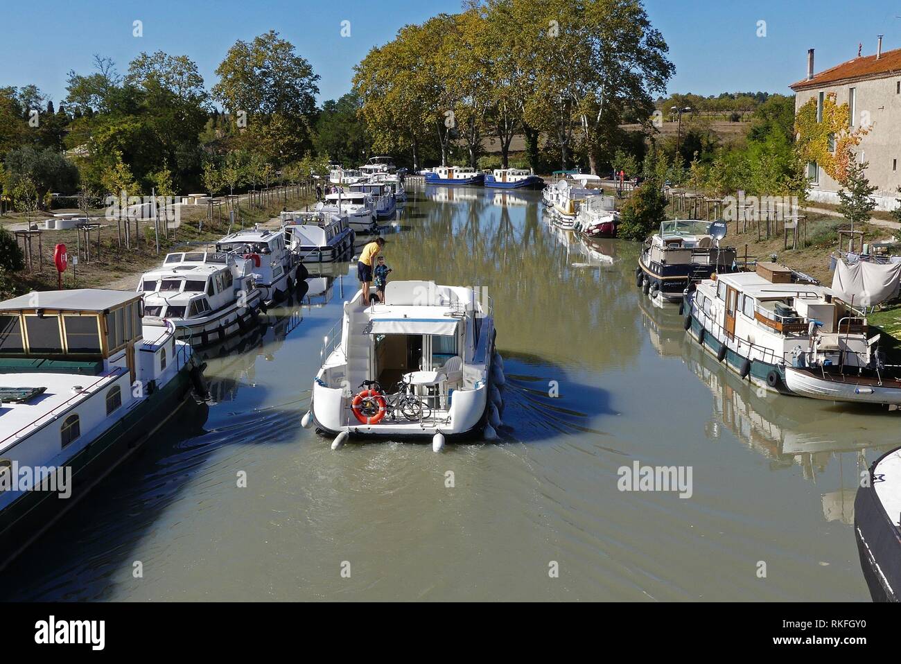 A father and son piloting a boat down the Canal du Midi at Capestang, France Stock Photo