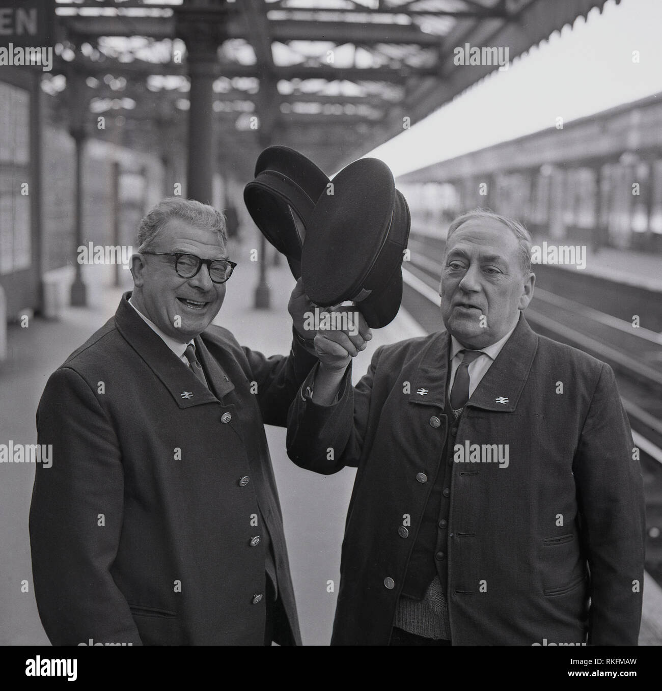 1968, two cheerful uniformed British Rail station staff, a foreman and ticket collector standing on a platform at Blackheath railway station, raise their caps, Blackheath, London, England, UK. Stock Photo