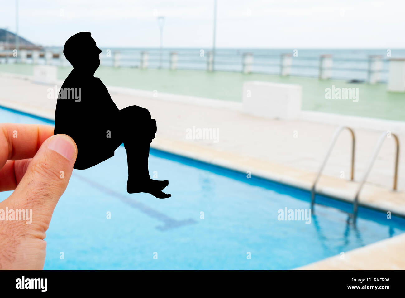 closeup of the hand of a man with a black paper cutout in the shape of a man throwing himself into a swimming pool Stock Photo