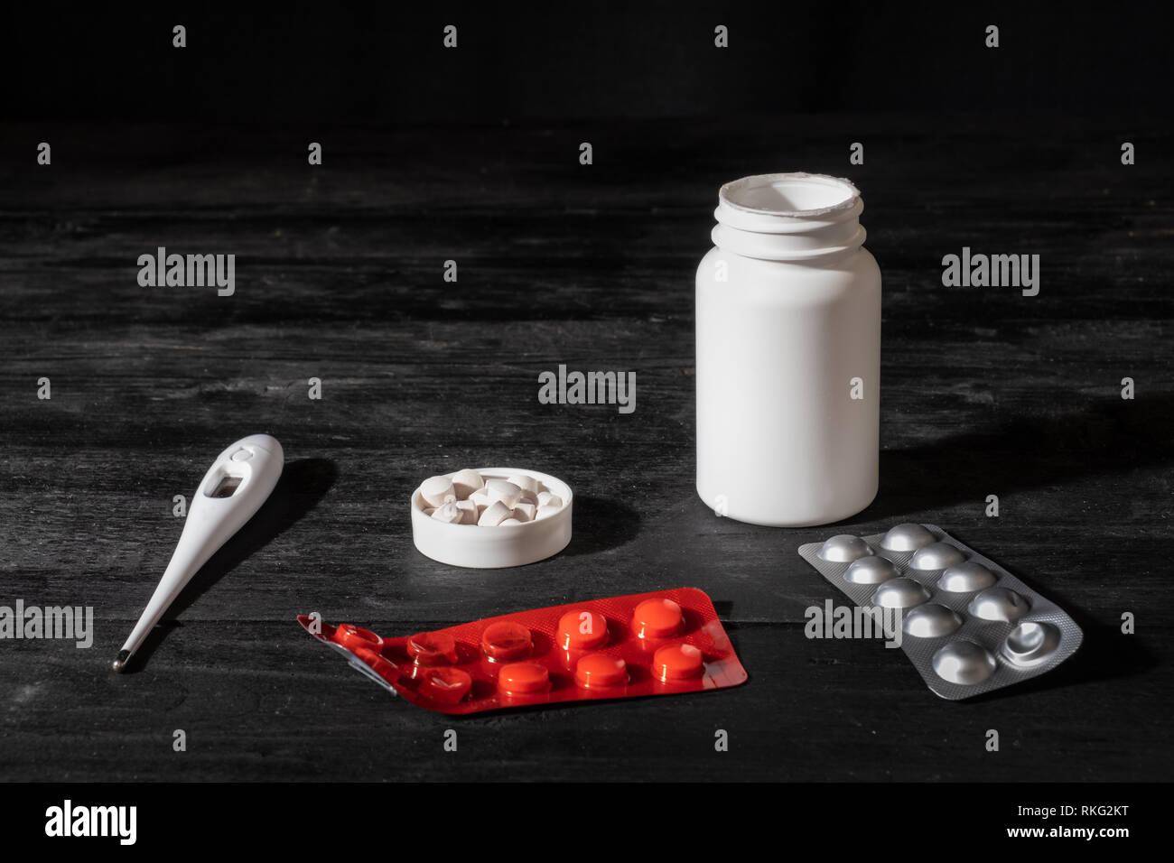 Medical pills and thermometer on black wood background. Self treatment concept: minimalistic low key image of prescription drugs. Stock Photo