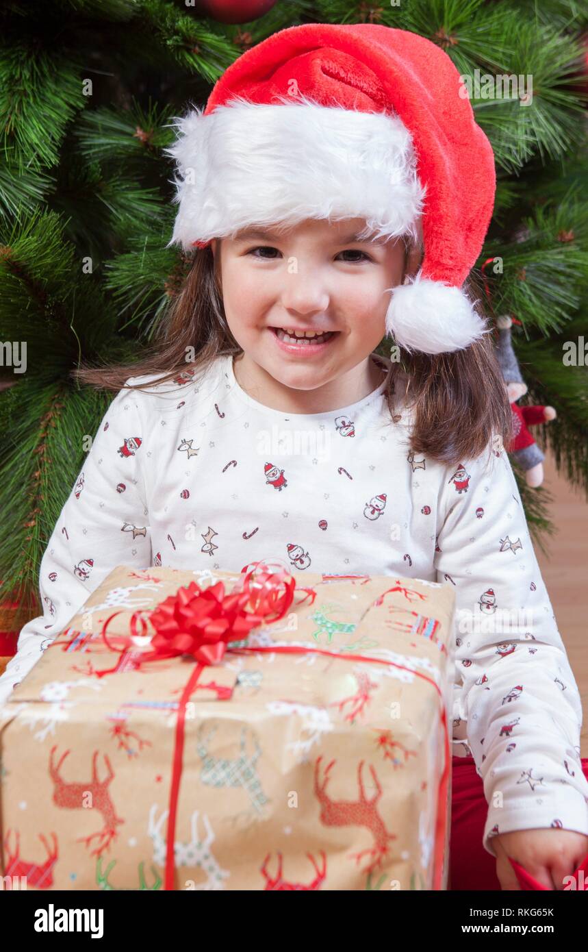 Joyful little girl child with her gift box under Christmas tree. She just have found her present. Stock Photo
