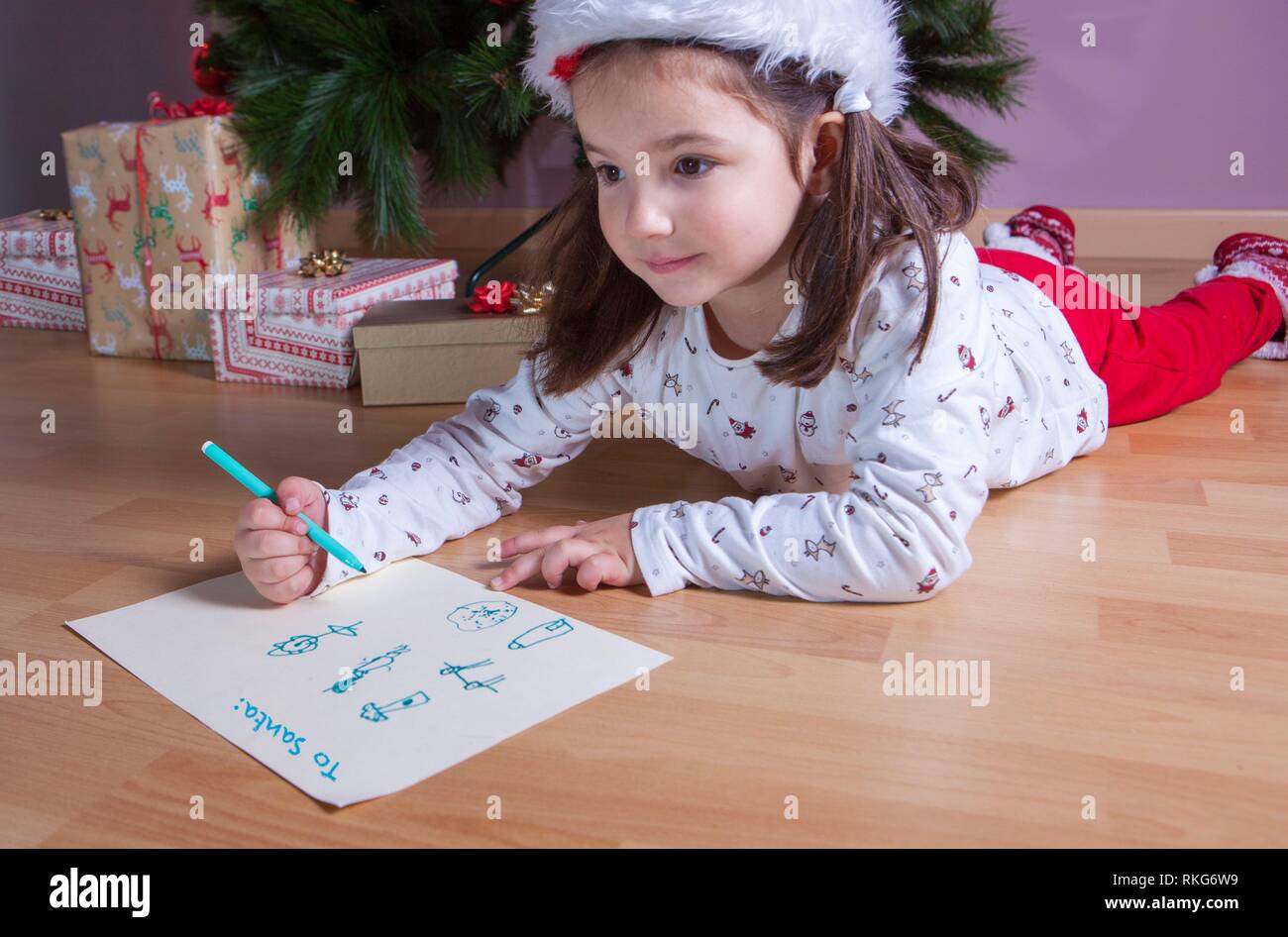 Little girl preparing the Santa Letter. She painting the gifts she want. Pre-reader concept. Stock Photo