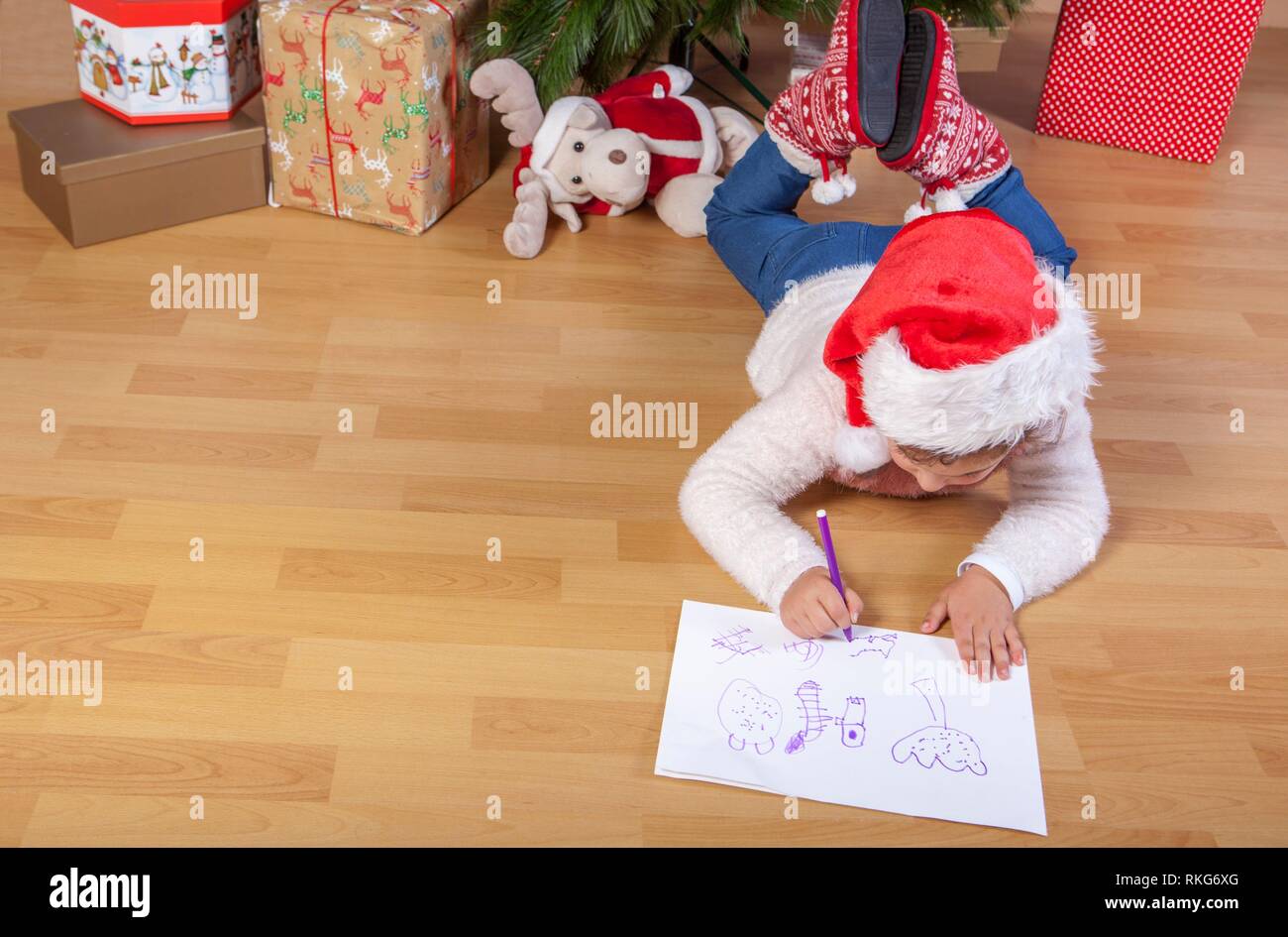 Little girl preparing the Santa Letter. She painting the gifts she want. Pre-reader concept. Stock Photo