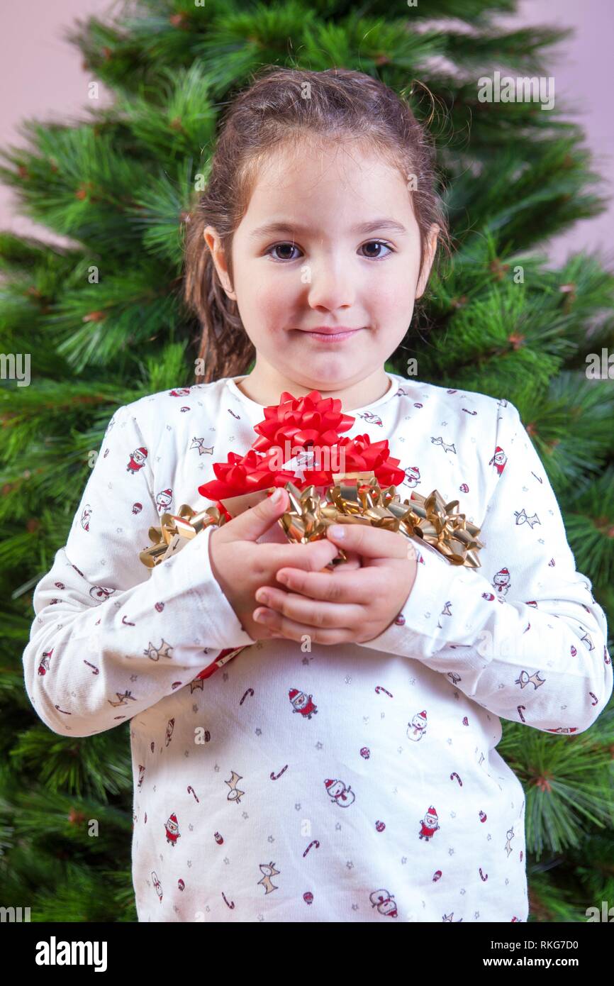 Merry Christmas and Happy New Year. Smiling little girl with a lot of ribbons for Christmas tree decoration. She is very, very happy. Stock Photo