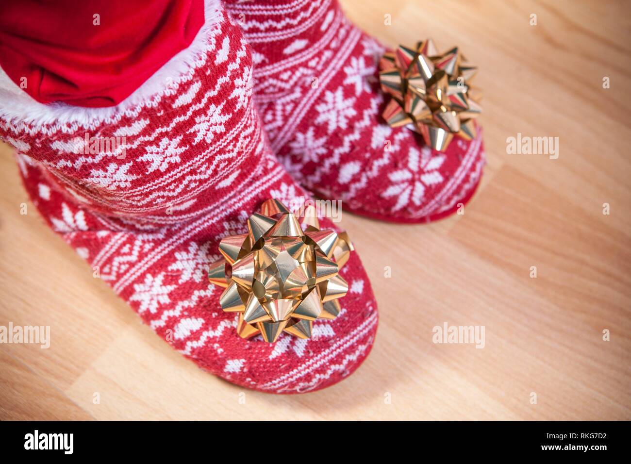 Red knitted boots with fur full of ribbons over wooden floor. Christmas staff concept. Stock Photo