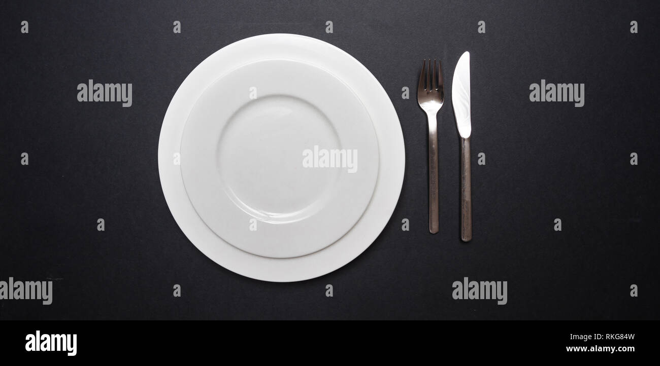Table place setting on black. Set of empty white plates and cutlery on black color background, top view, copy space Stock Photo