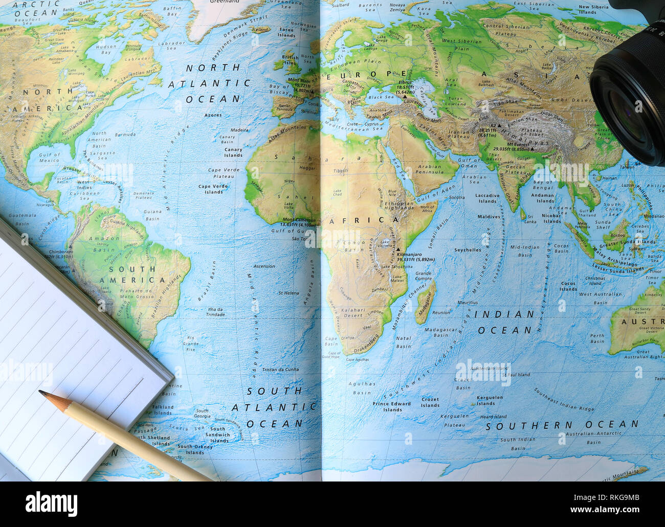 Lined Notebook with White Pencil and Camera on the World Map Stock Photo