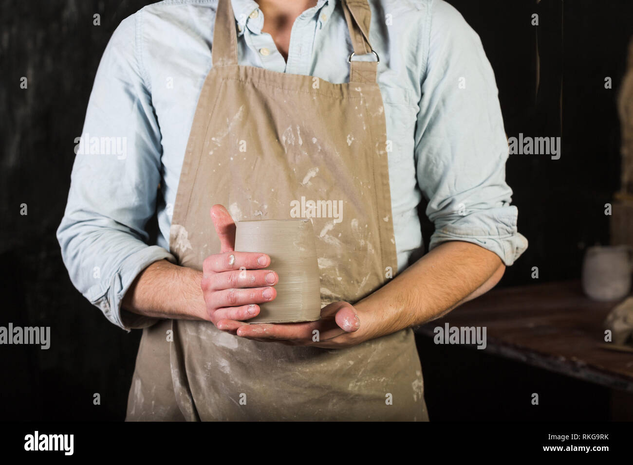 Potter wearing apron stained with clay and shirt holding a clay jug. Front view, closeup. Art and hobby and freelance working concept. Stock Photo