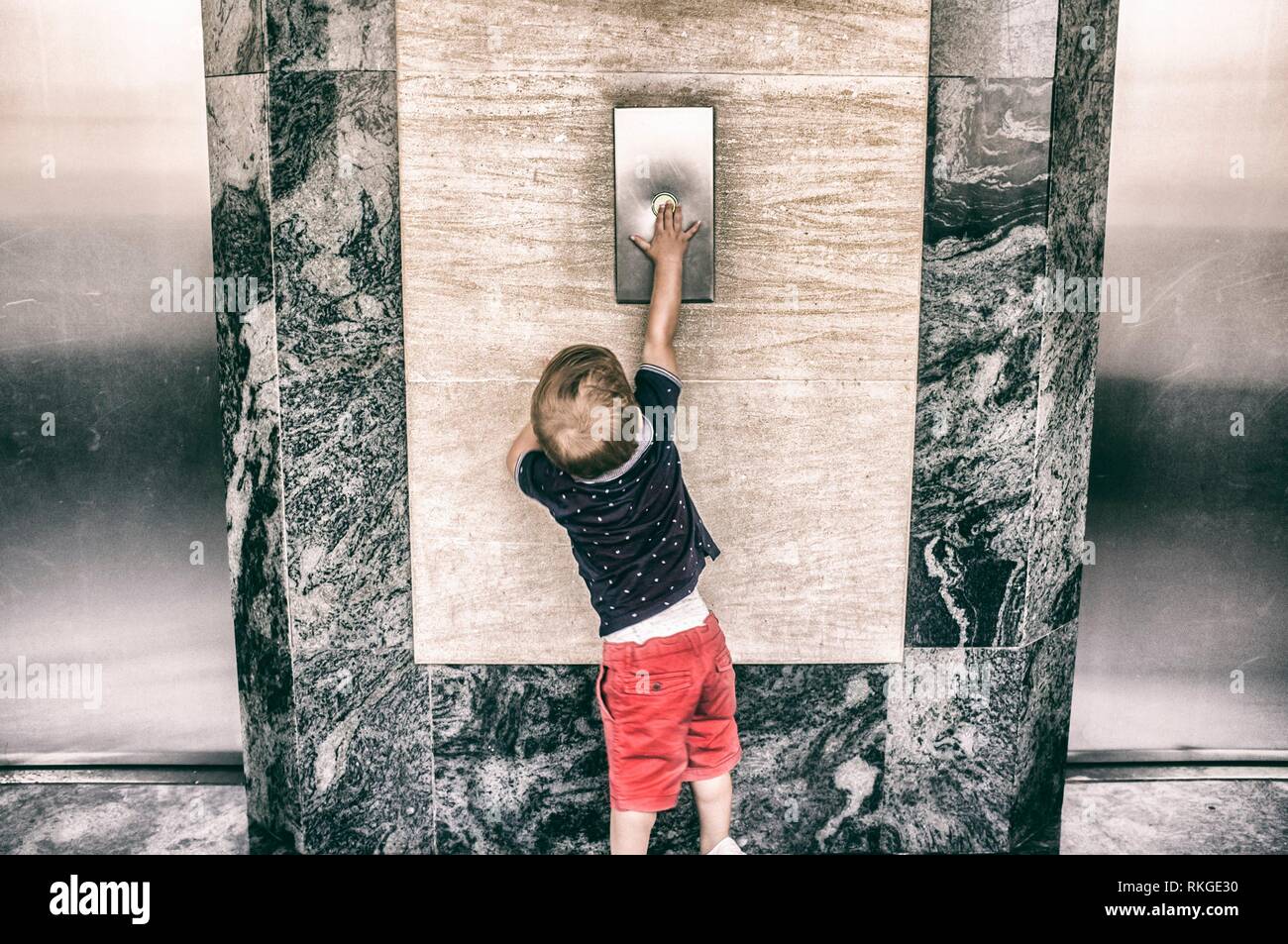 Toddler boy calling elevator button. Vintage filtered. Stock Photo