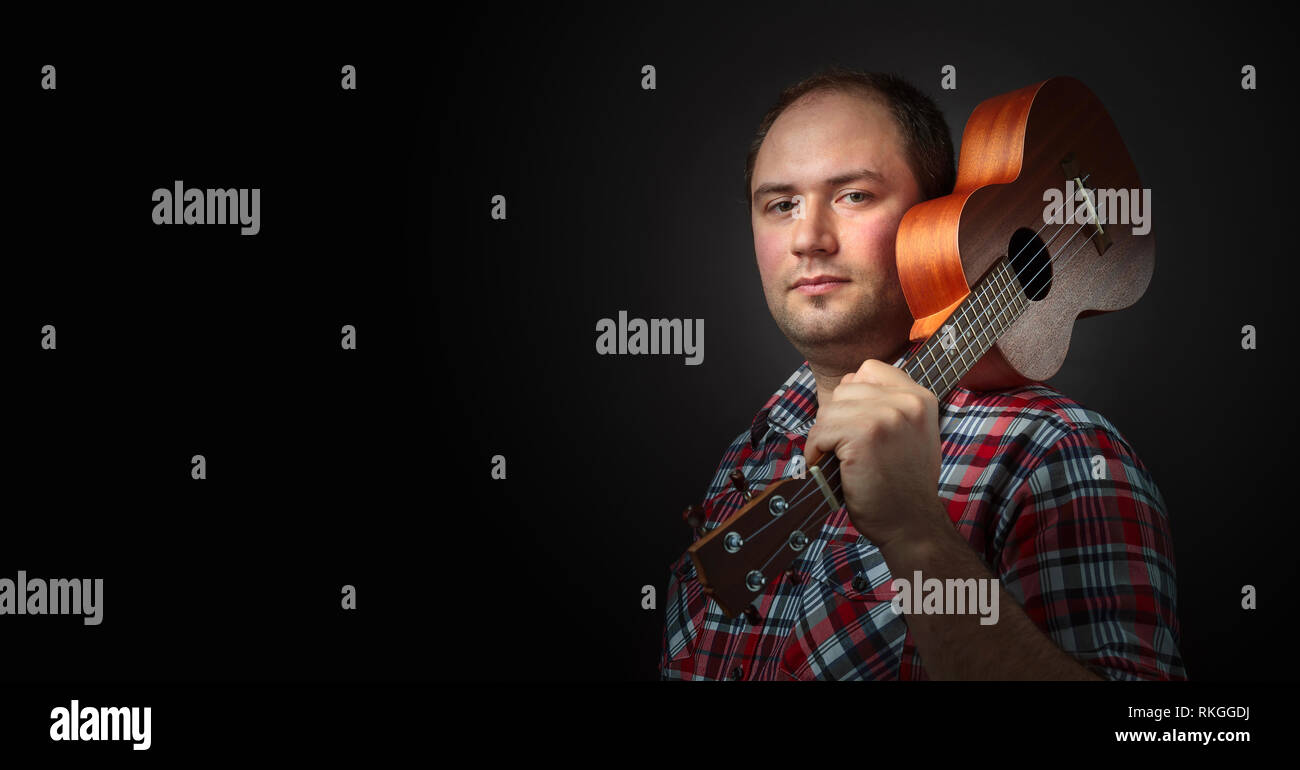 Male musician with ukulele. Backlighting, dark background. Copy space ...