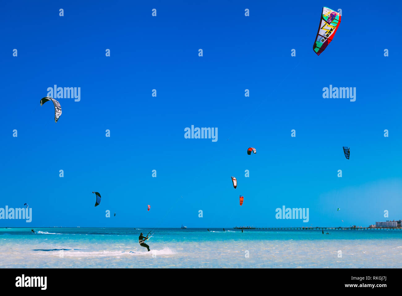 Egypt, Hurghada - 30 November, 2017: Numerous flying kites in the blue sky over the Red sea surface. The professional kitesurfers gliding on the waves Stock Photo