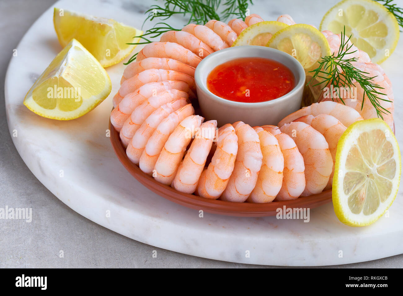 Close-up on shrimp ring with sweet chili sauce on marble serving board on light table Stock Photo