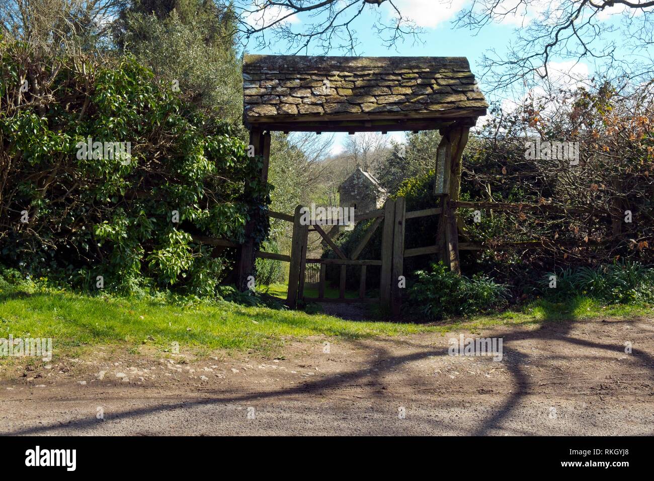 Spring sunshine on the picturesque lychgate to the tiny old Saxon church at Duntisbourne Rouse in the Cotswolds, Gloucestershire, UK. Stock Photo