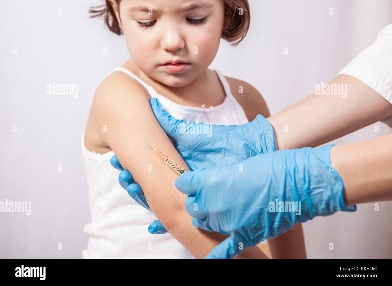 Nurse vaccinating 3 years old little girl. She is worry about painful stitch. Stock Photo