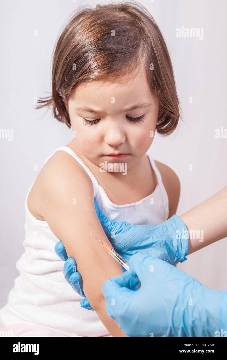 Nurse vaccinating 3 years old little girl. She is worry about painful stitch. Stock Photo