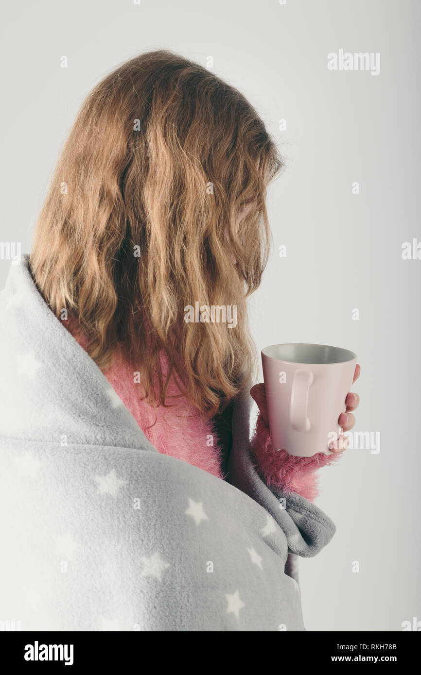 Young woman has caught cold, has day off, sick day, wrapped in blanket, holds cup of herbal tea. Profile portrait view Stock Photo