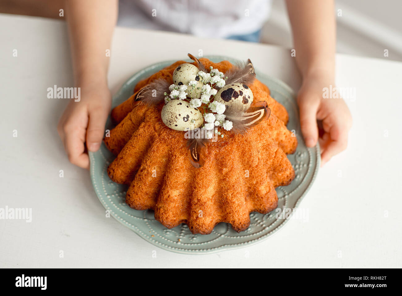 Little girl's hands hold a plate with easter cupcake decorated with easter eggs and feathers. Breakfast Stock Photo