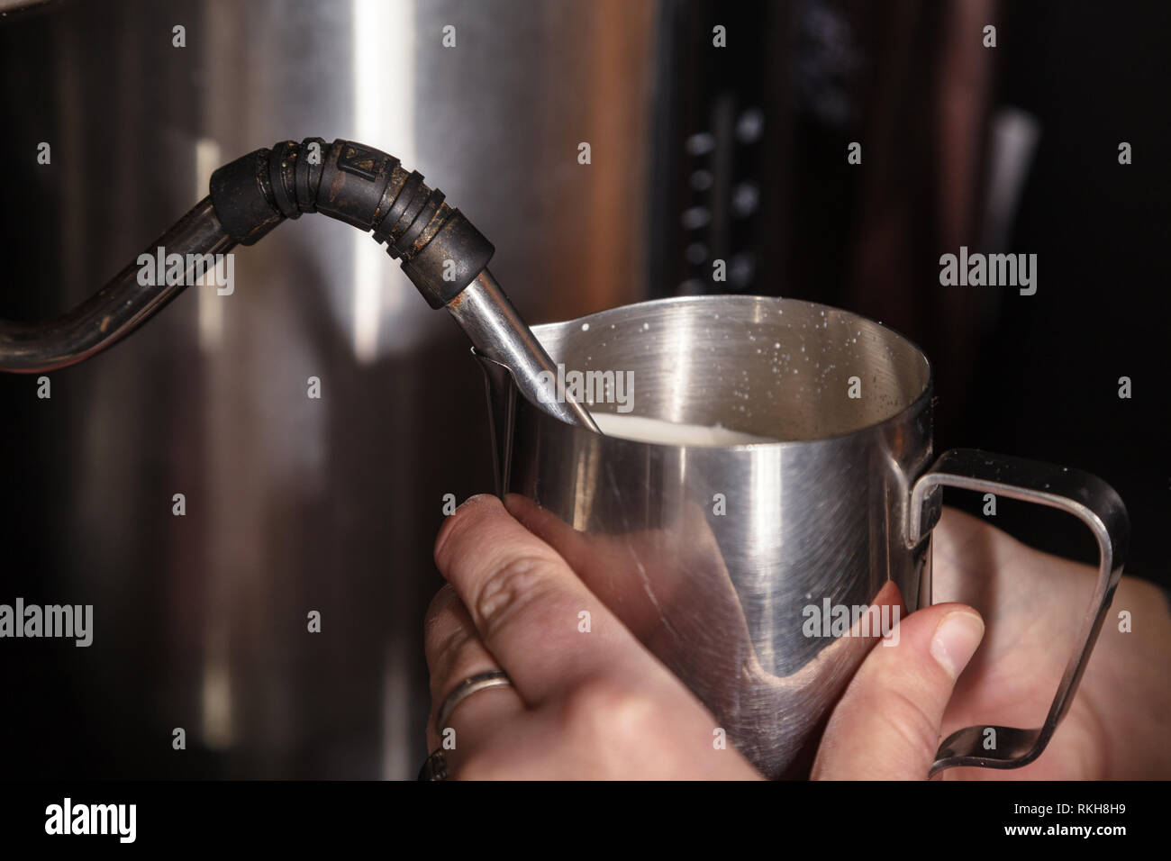 A barista at a cafe churns milk in a metal jug using a caper of professional coffee machine
