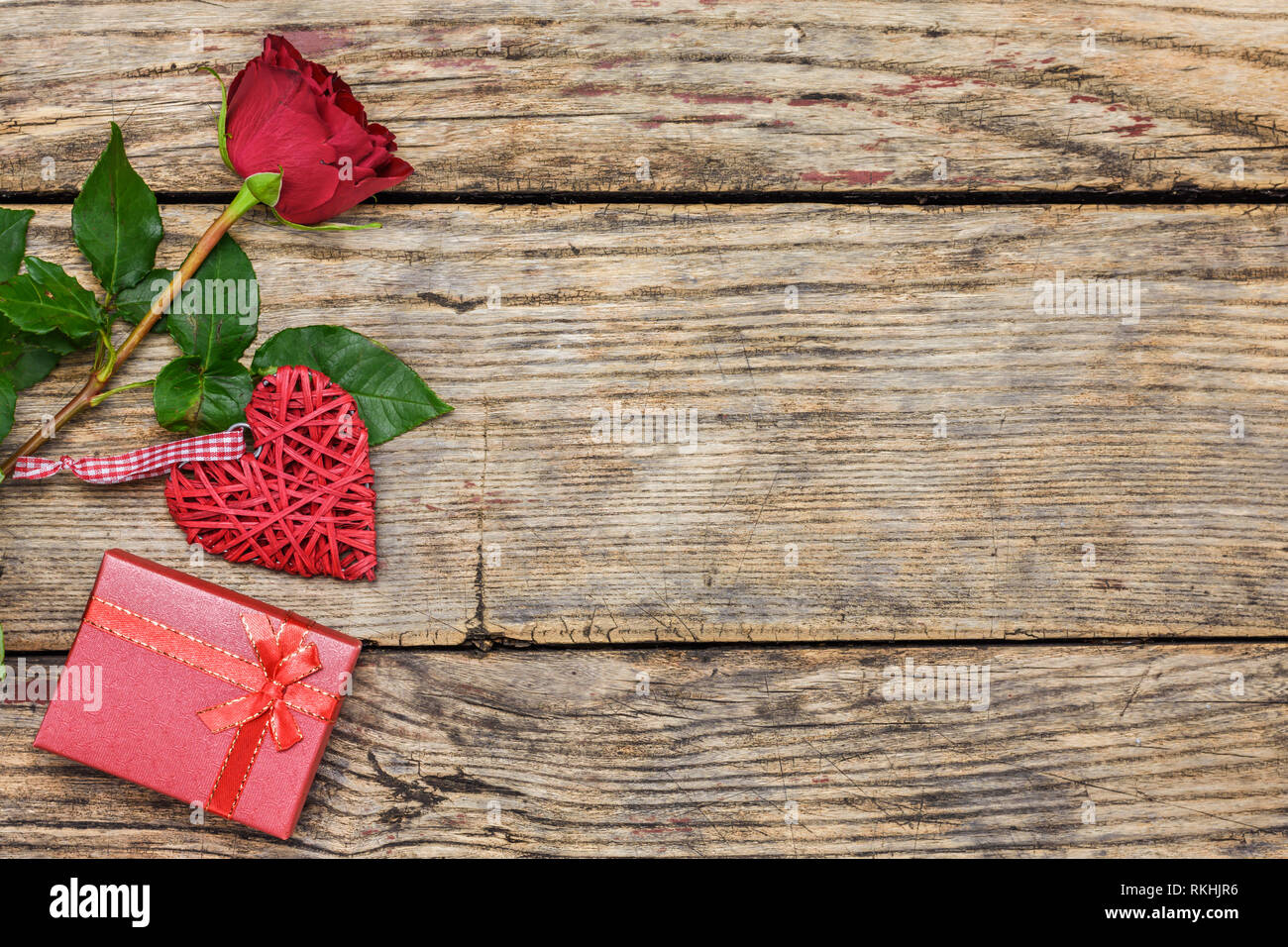 Valentines day concept. Red rose, gift box and wicker heart on a rustic ...