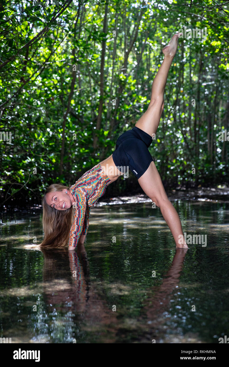 Young woman practicing yoga (Downward Facing Dog Split (Three-Legged Dog) in a natural setting - Fort Lauderdale, Florida, USA Stock Photo