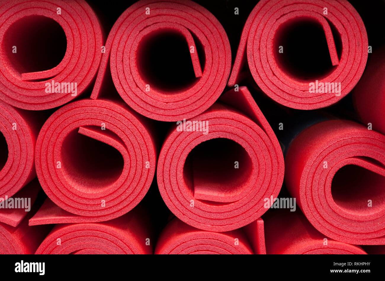 Lot of rolled up red foam fitness mats background. Travel and sport. Stock Photo
