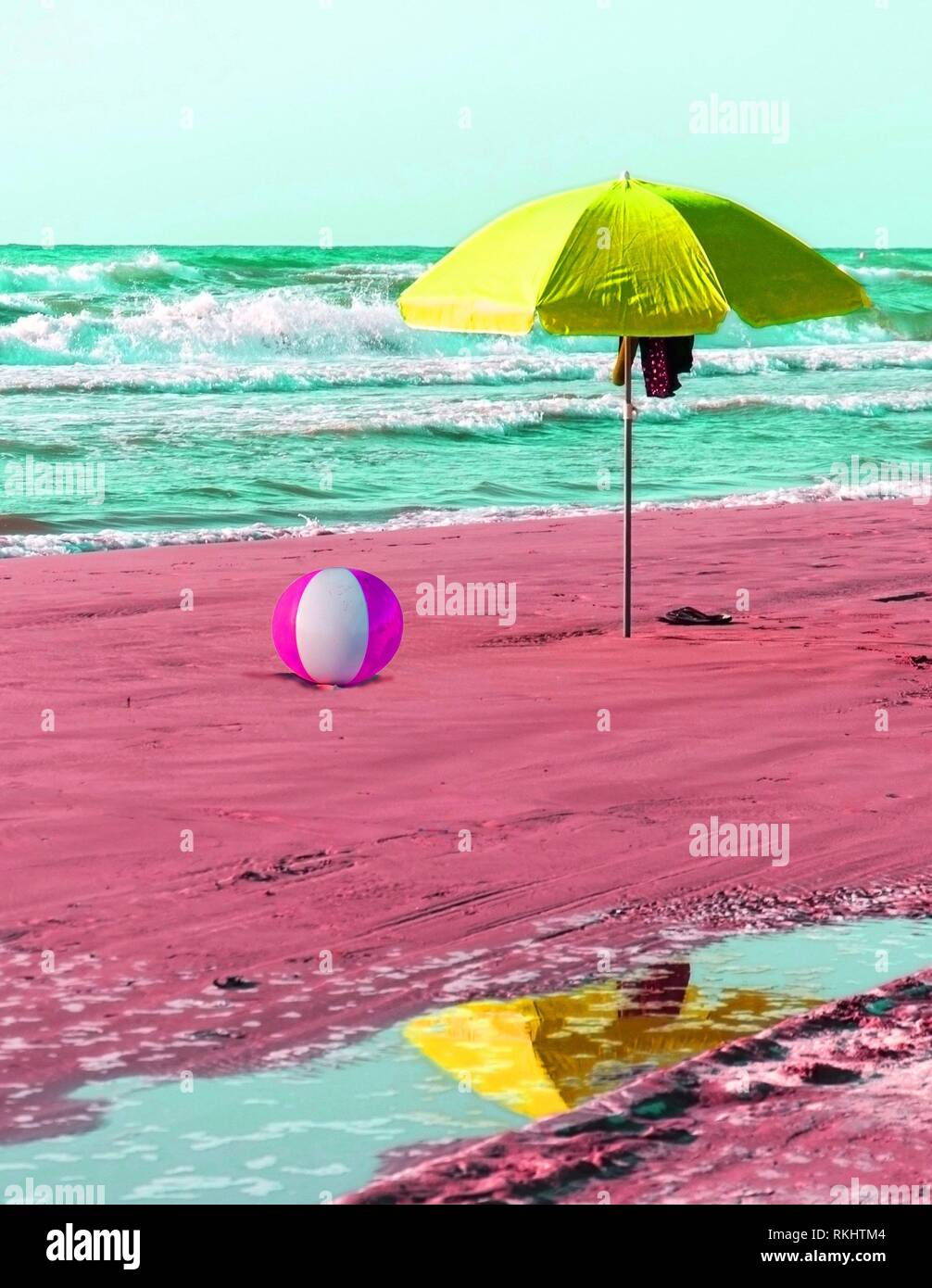 Fun beach concept with parasol, shoes and inflatable ball in surrealistic colours. Stock Photo