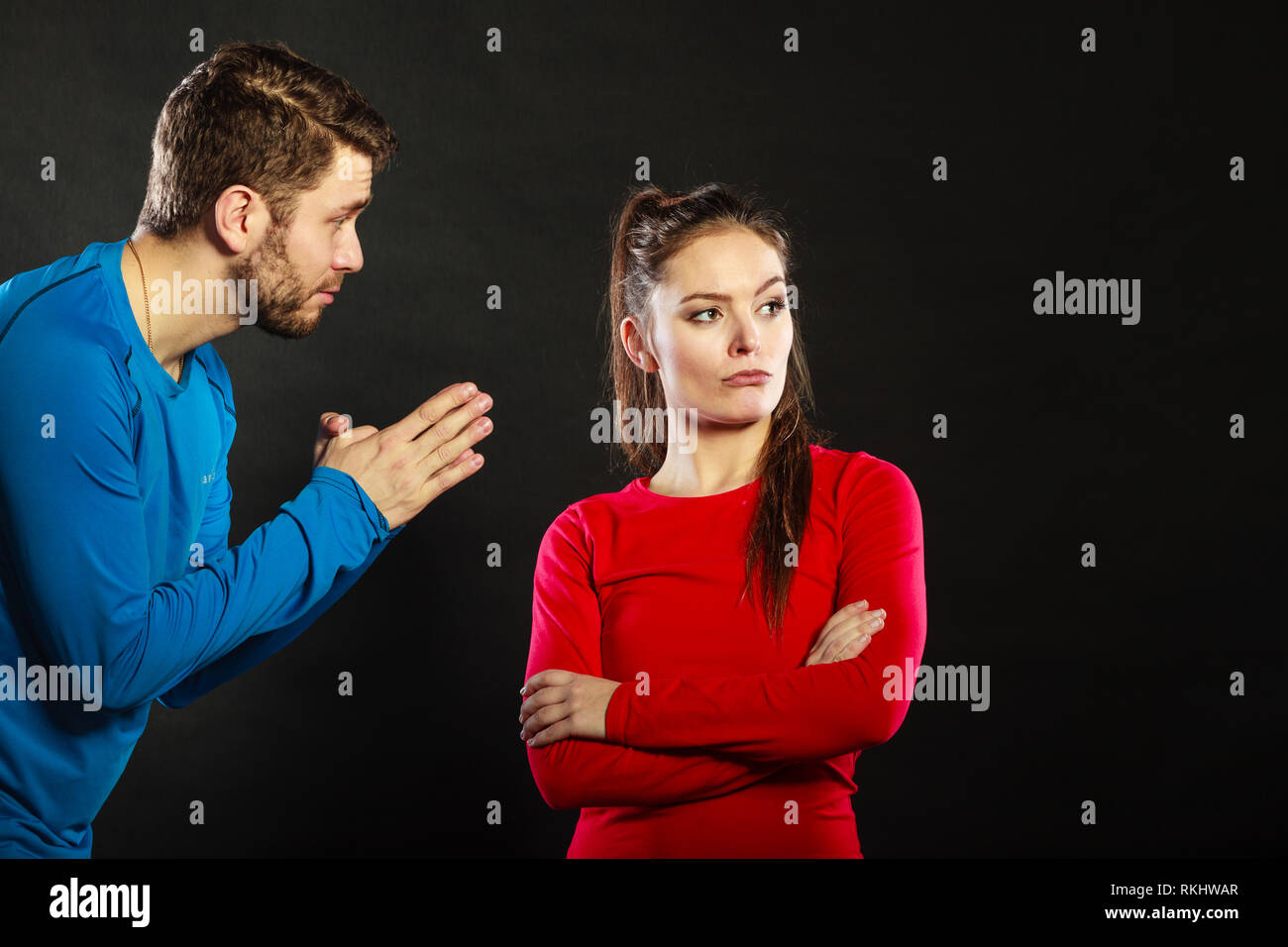 Husband apologizing upset angry wife. Man asking woman for forgivness. Boyfriend trying to convince girlfriend. Conflicted couple in studio on black.  Stock Photo