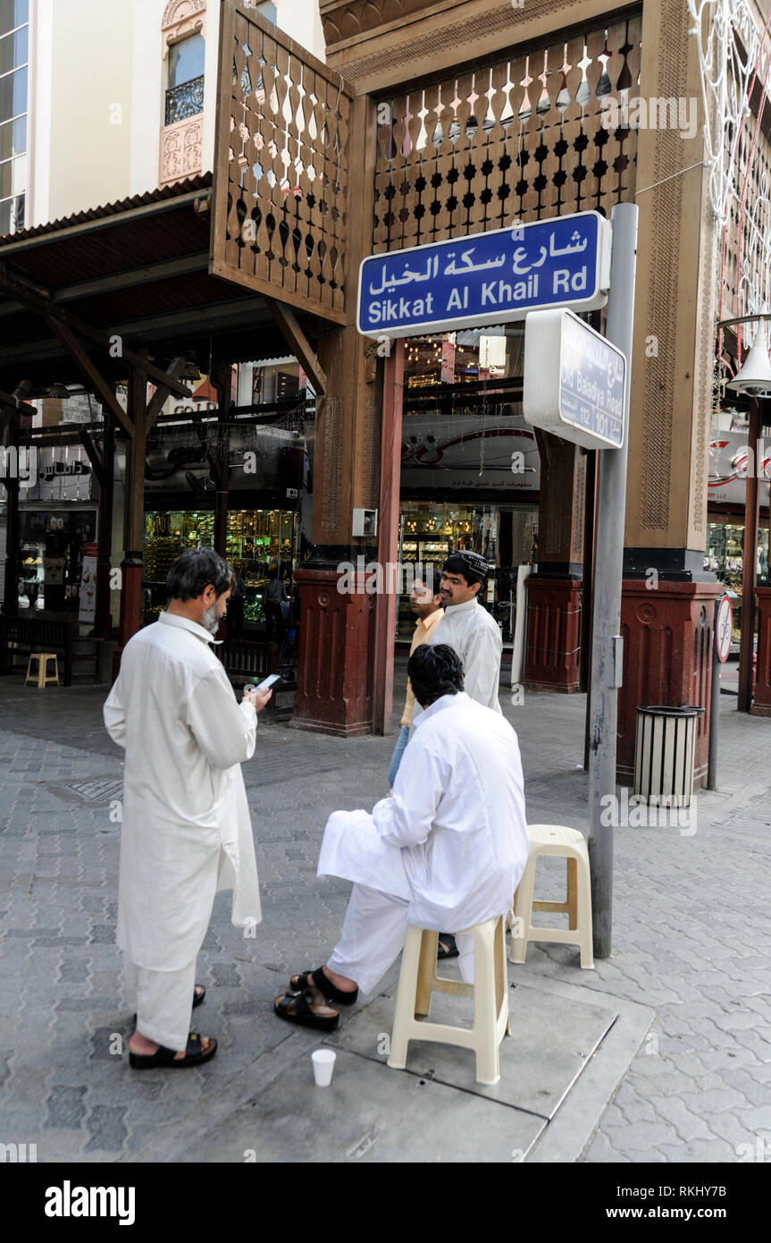 Three Asian retailers outside the one of the main wooden structure  entrances to the Dubai Gold Souk in the district of Deira in Dubai in the  United A Stock Photo - Alamy