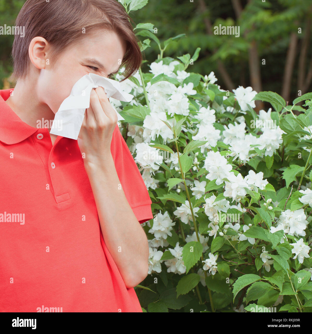 Teenager boy with seasonal influenza blowing his nose on a tissue in a