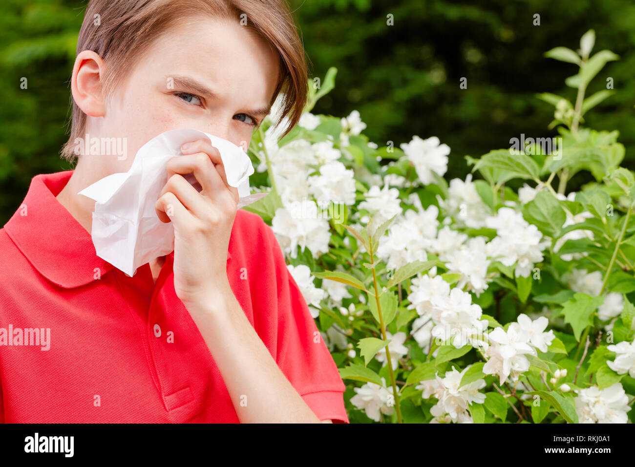 Teenager boy with seasonal influenza blowing his nose on a tissue in a
