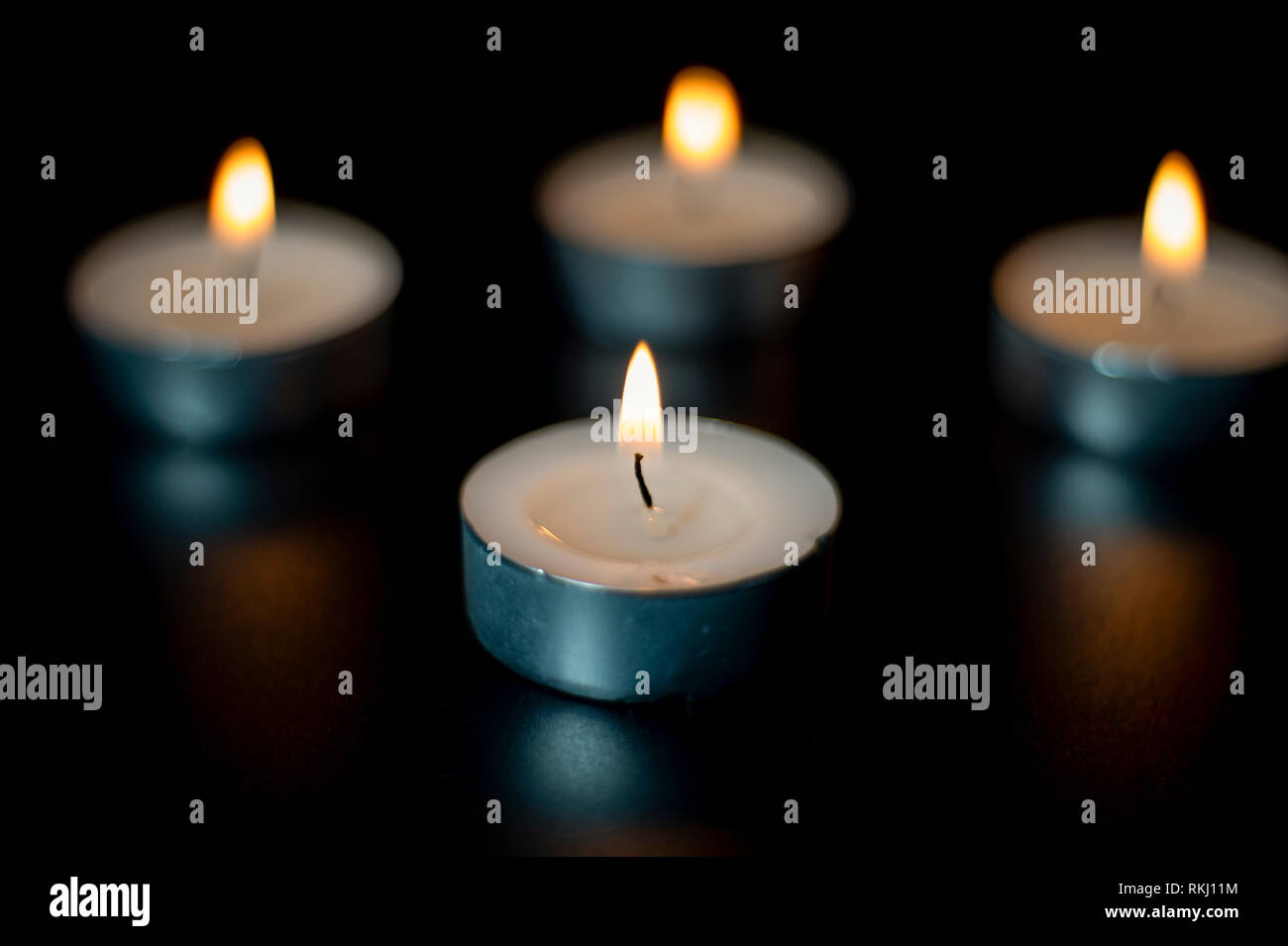 Four tea candles with reflection on black background. Selective focus. Stock Photo