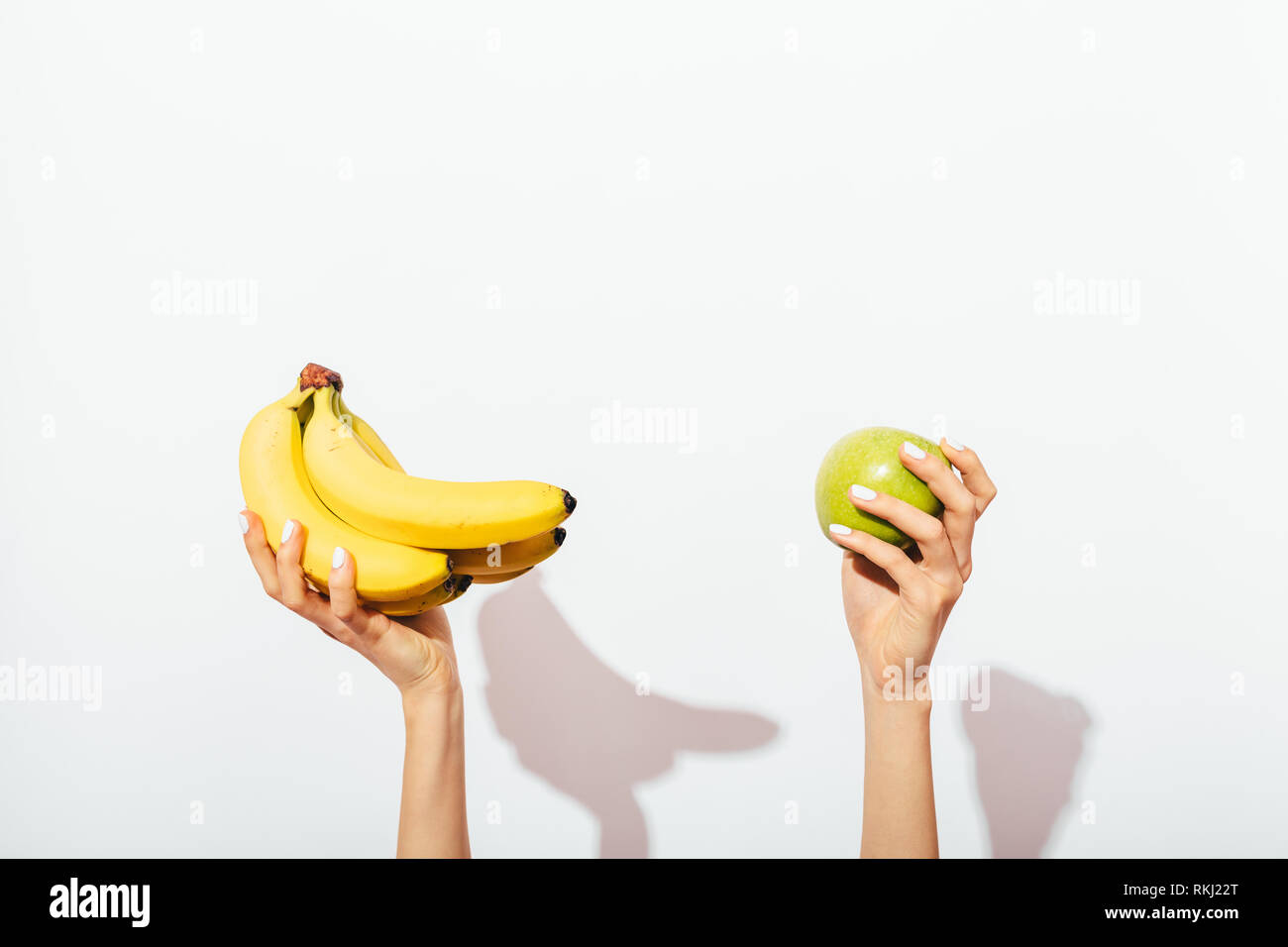 Female's hands with manicure holding bunch of bananas and green apple on  white background, casting shadows Stock Photo - Alamy