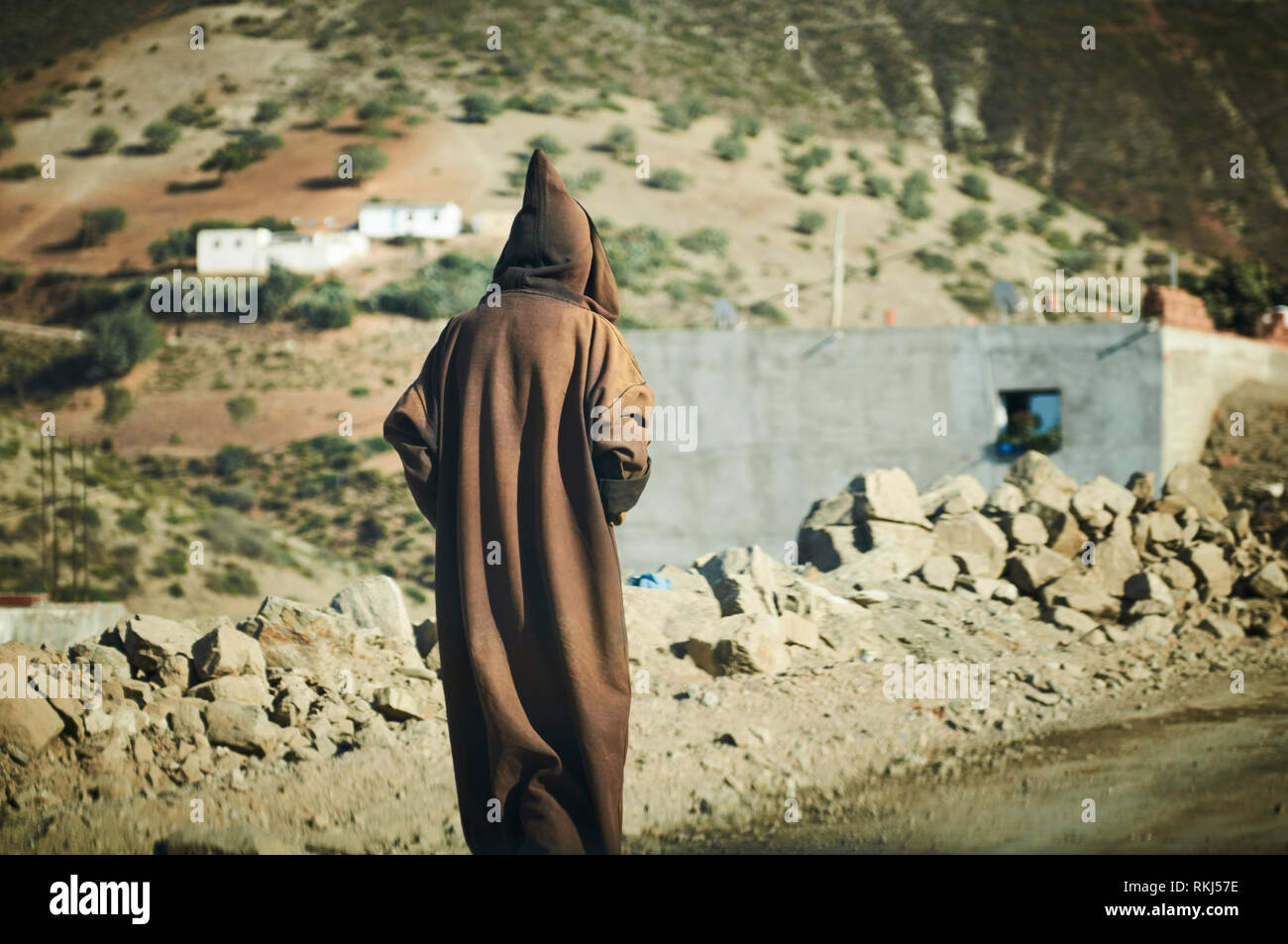 A man wearing a hooded robe called a djellaba or thoub walks along the side  of the road just outside of the town of Chefchaouen Stock Photo - Alamy