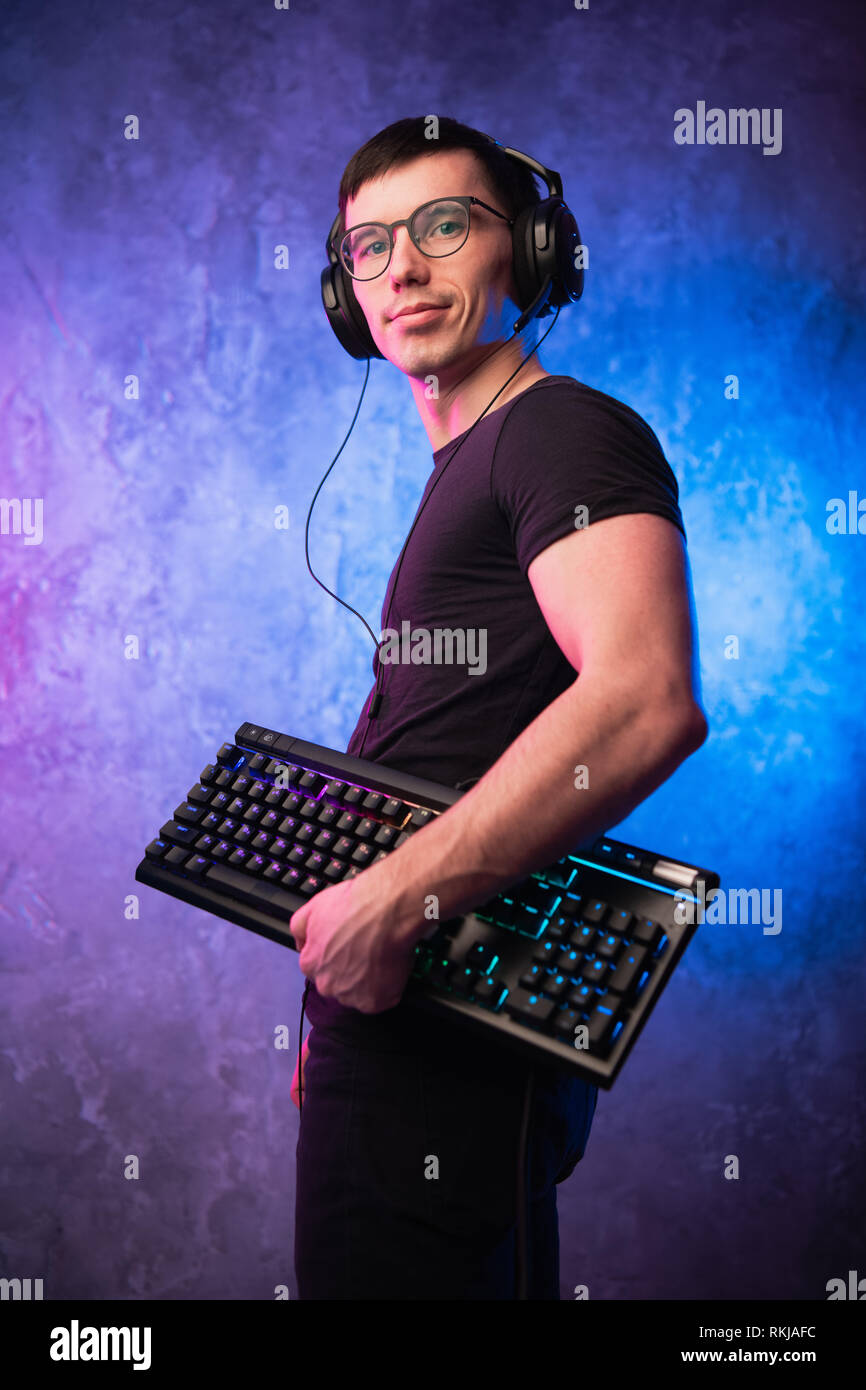 Computer nerd with keyboard over colorful pink and blue neon lit wall Stock Photo